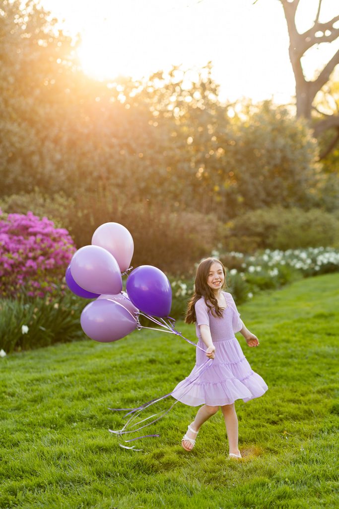 Nine-year-old girl spinning in a field with purple and lavender balloons during her outdoor birthday photo session