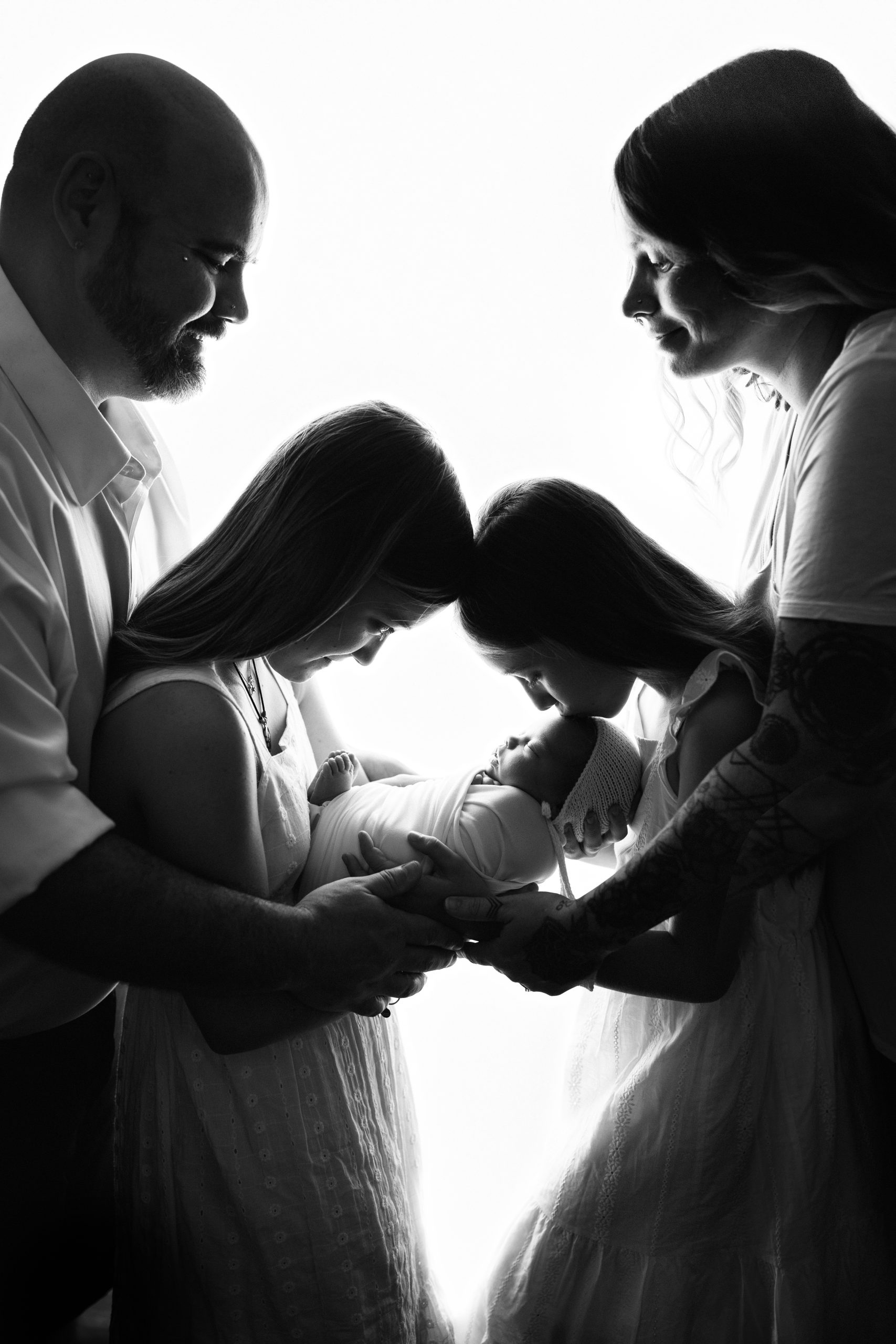 Tender silhouette moment of big sister kissing baby during newborn session family portrait