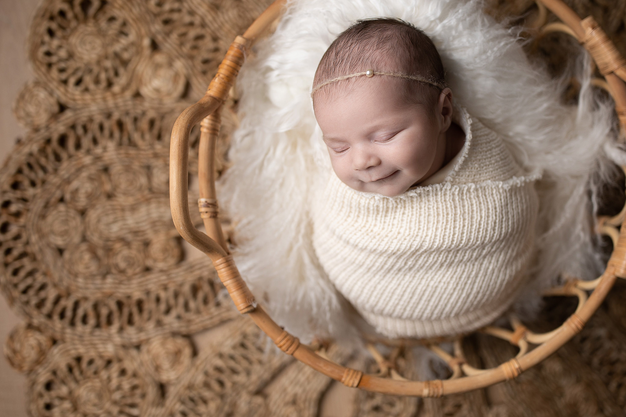 sleepy smiles from a newborn baby in a basket wrapped in a cream knit blanket