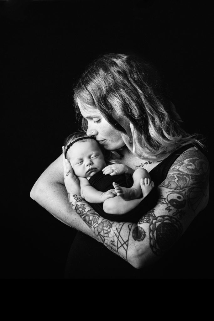 black and white portrait of a mom with tattoos holding her newborn baby girl in her arms