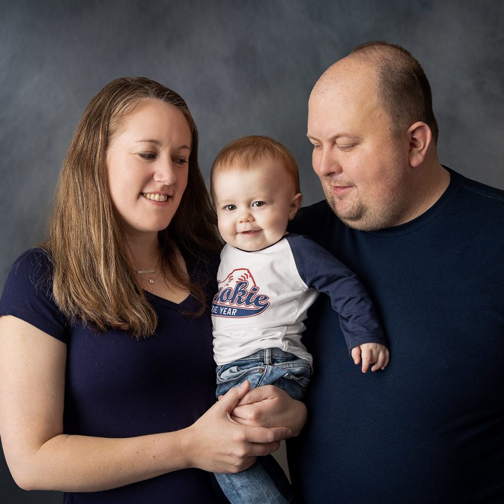 grinning one-year-old with parents at birthday photo session