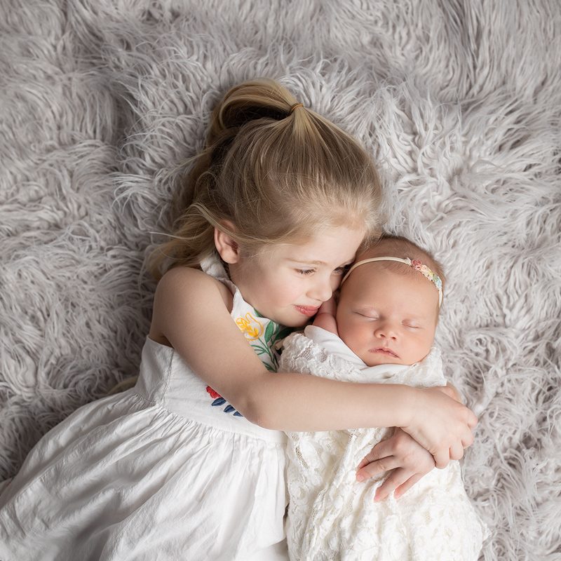 big sister hugs newborn baby girl in sweet photo