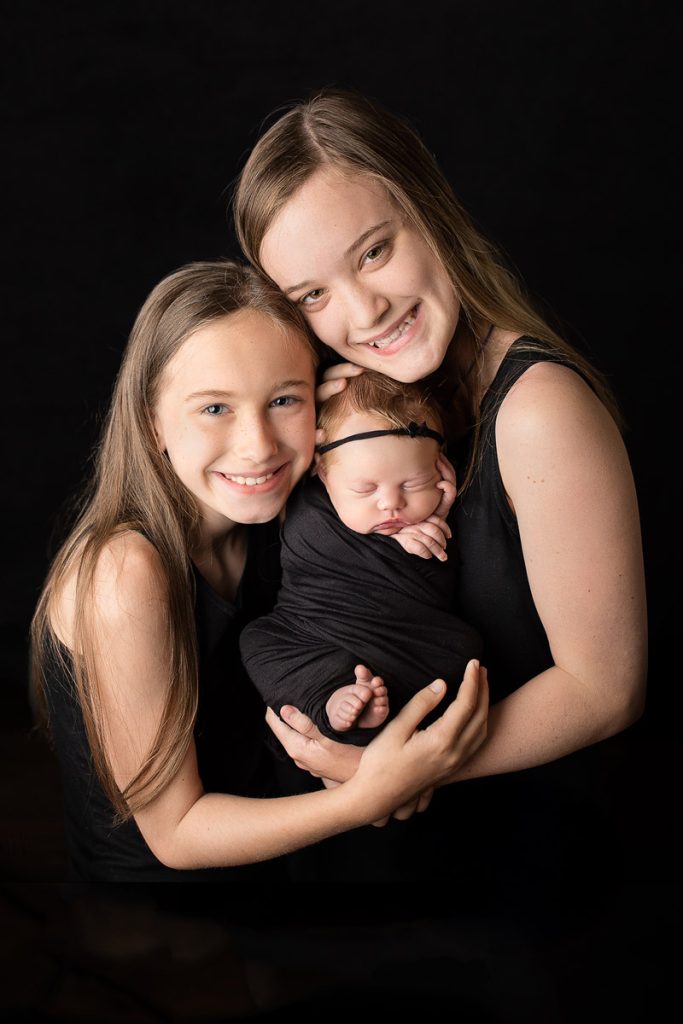 big sisters bonding with new baby girl wearing black