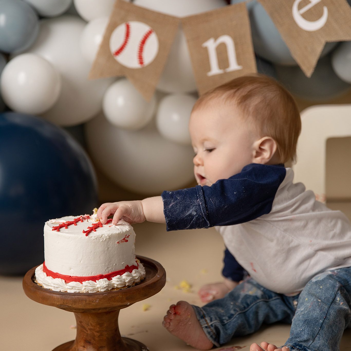 Close-up of baby’s hand reaching toward a birthday cake during a vintage baseball-themed first birthday session, capturing curiosity and tiny fingers.