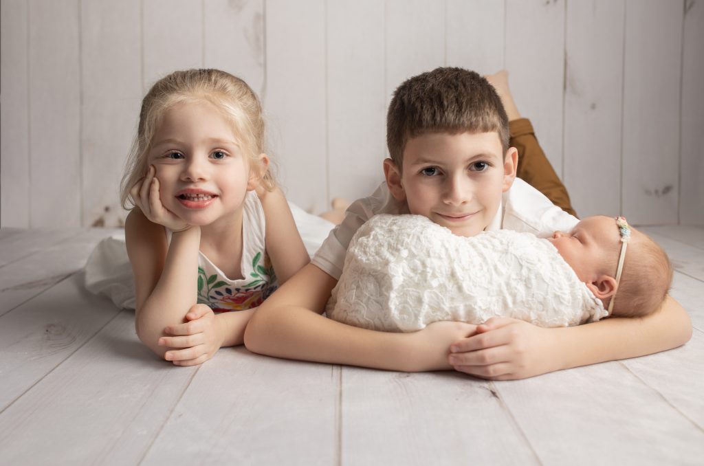 Older siblings smiling while holding baby sister during family portrait