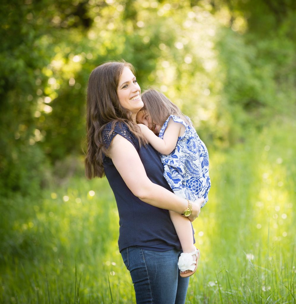 Mom holding her two-year-old daughter during a golden hour birthday photoshoot in a grassy field, both smiling and connected in a sweet moment