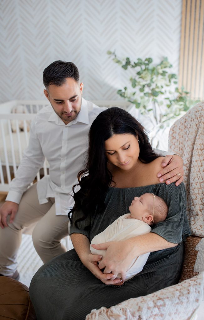 New parents snuggling their newborn baby in a cozy boho nursery with soft natural light