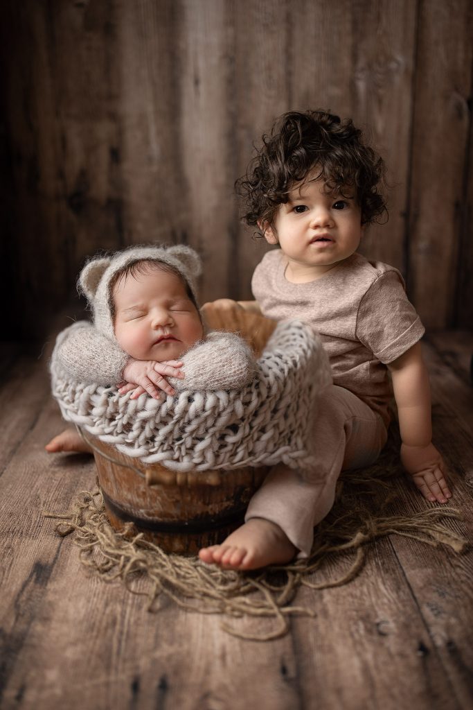 toddler sibling with baby in a bucket with parents closeby for safety