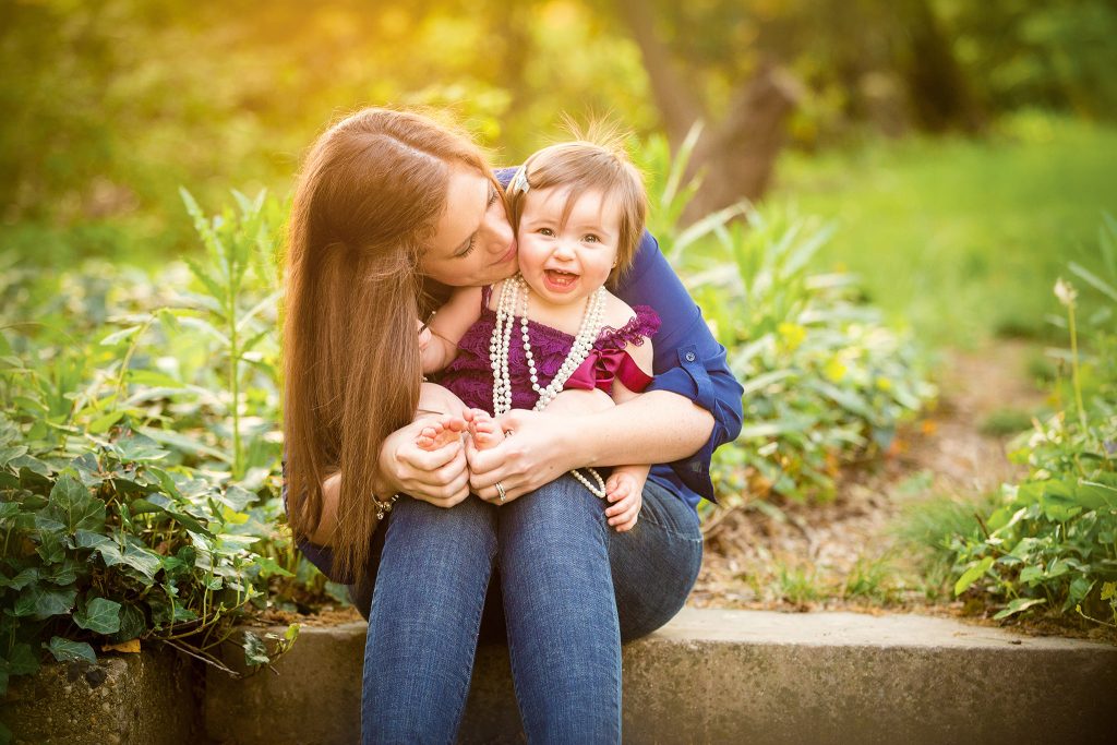 Smiling baby in mother’s arms during golden hour at an outdoor birthday session