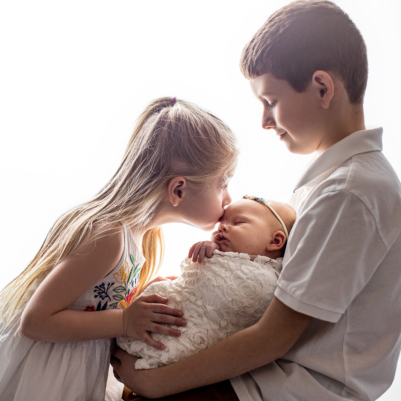 Big sister kissing baby sister with older brother during in-home newborn session