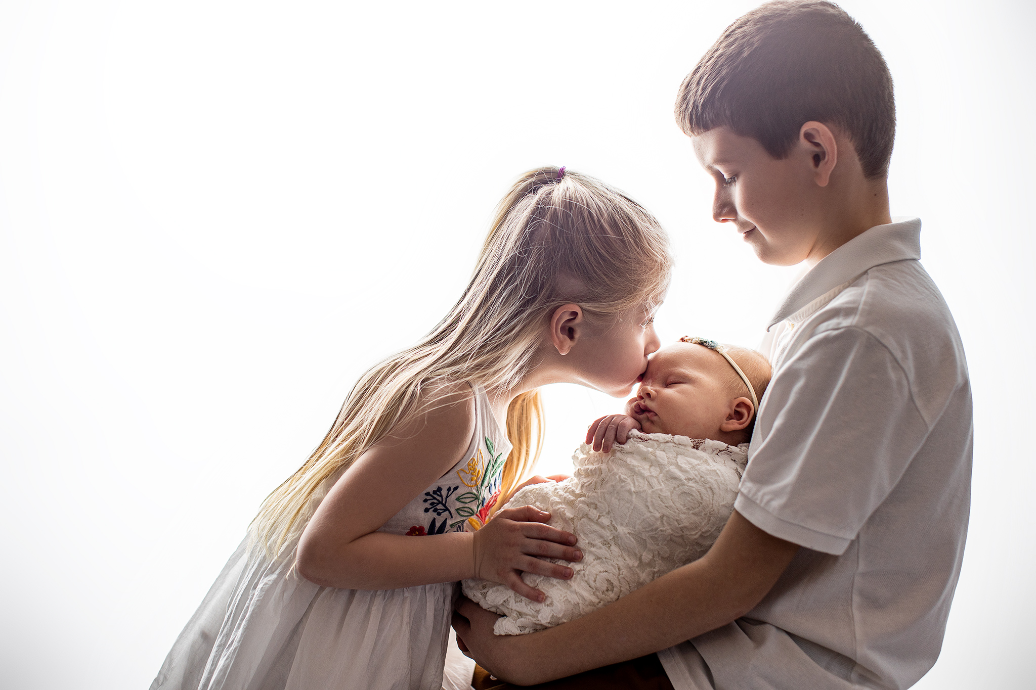 Big sister kissing baby sister with older brother during in-home newborn session