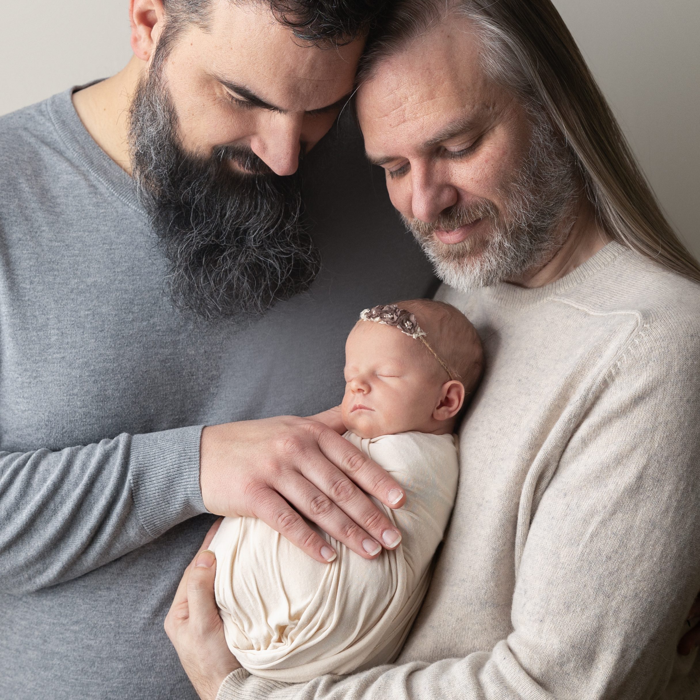 2 dads holding newborn baby girl in cream and gray.