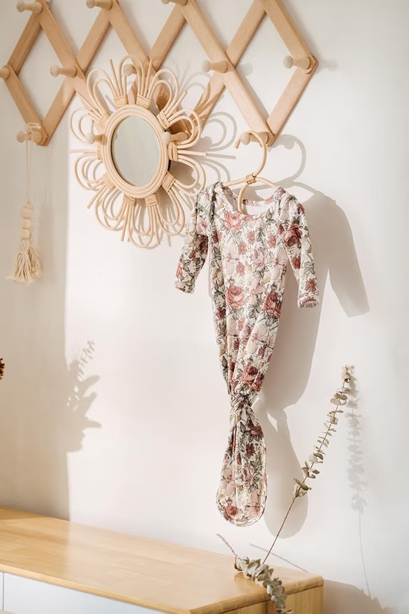 Floral newborn gown with a knotted hem, hanging on a hanger